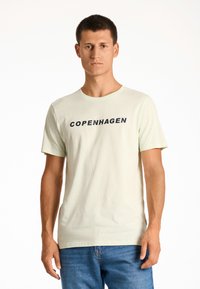 Camiseta de algodón verde claro con cuello redondo y mangas cortas, con "COPENHAGUE" impreso en letras negras en negrita a lo largo del pecho.