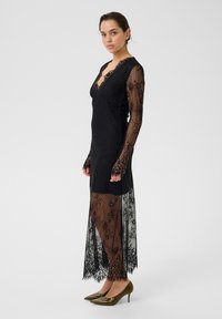 Must mustrehemeline must kõrvadega, mis sisaldab keerulisi lillemustreid, V-dekoltee, vormitud kehaosa ja läbipaistev ääreosa, koos roheliste kõrvarõngastega.