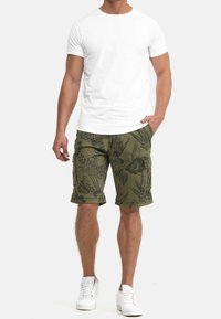 Vit t-shirt med rund hals ringad, kombinerad med olivgröna cargoshorts med blommönster och sidofickor. Modellen har på sig vita sneakers.