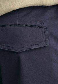 Marineblaue Hose mit einer hinteren Tasche in Diamantform, feiner Textur und gesticktem "GANT"-Logo in passender Farbe.