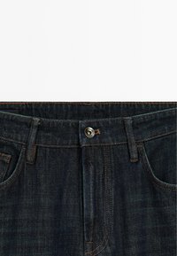 Dunkelblaue Jeans aus Denim mit Knopfverschluss, sichtbaren Nähten und Fünf-Taschen-Design. Der Stoff hat eine leichte Textur und eine dezente Ausbleichung.