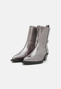 Botine din metal argintiu, cu vârful ascuțit, fermoar pe lateral și toc mic tip bloc. Construită dintr-un material sintetic neted și strălucitor.