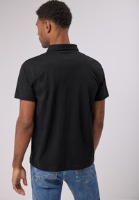 Mustapaitainen lyhythihainen polo-paita, jossa on kaulus, rento istuvuus ja pehmeä rakenne. Yhdistetty vaaleansinsisiin farkkuihin.