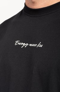 Black cotton t-shirt with a high neckline featuring white embroidered text "Energy never lies" on the chest. Smooth texture, casual design.