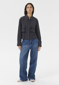 Hemd mit Karomuster, in dunkler Ausführung, mit zwei aufgesetzten Brusttaschen, Knopfleiste und langen Ärmeln; kombiniert mit weiten blauen Jeans.