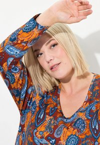 Mehrfarbiges Langarmoberteil mit Paisleymuster in Blau-, Orange- und Burgunder-Tönen; V-Ausschnitt-Design; weiche Textur.