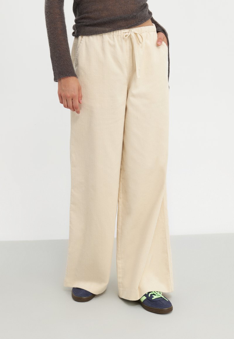 Lichtbeige wijde broek van textuurstof met een geribbeld patroon, voorzien van een drawstring taille en zijzakken.