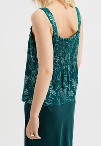 Teal topp med ett blommönster, samlad söm på baksidan, breda axelband och en avslappnad passform. Slät textur, i kombination med en matchande kjol.