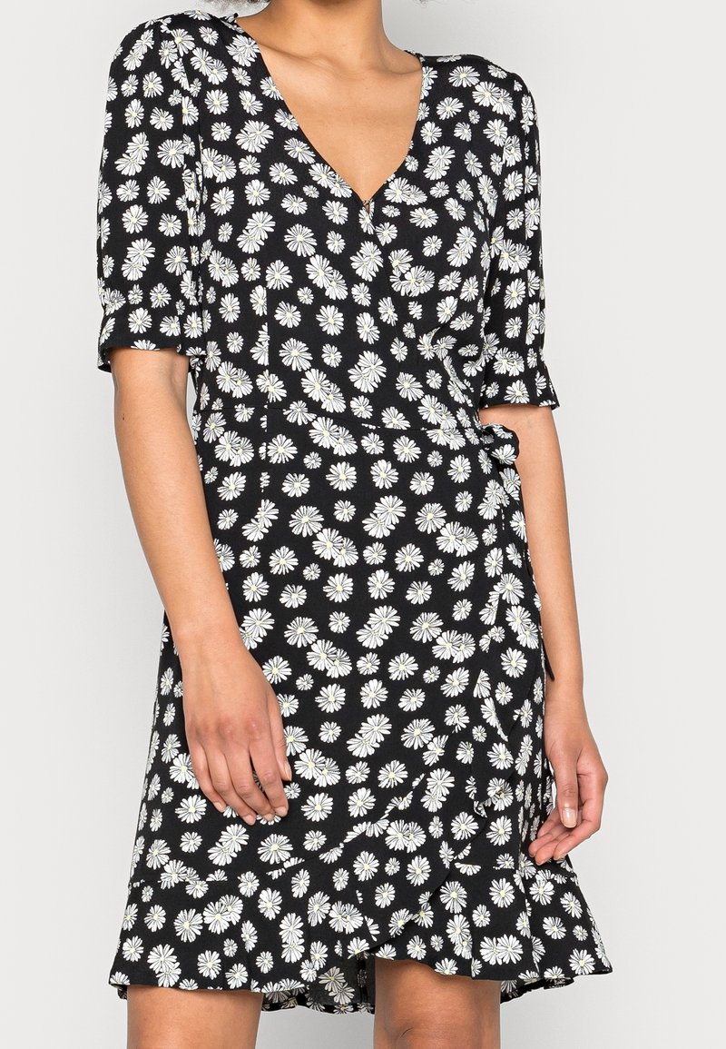 Robe noire à manches courtes avec imprimé marguerite blanc. Décolleté en V et ourlet évasé avec un lien à la taille. Tissu léger.