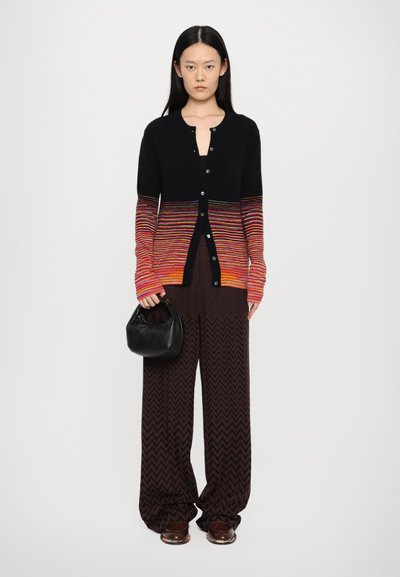 Knitted cardigan with a black body, transitioning to multicolored stripes in red and orange. Paired with brown chevron-patterned pants.