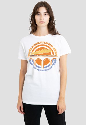 Young woman wearing white T-shirt with orange and blue Hogwarts Express train crossing a bridge and text "Away for the holidays"