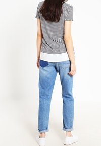 Camiseta de rayas blanco y negro, jeans de mezclilla azul, puños enrollados y zapatillas blancas. Vista trasera, corte informal, detalles de costura claros.
