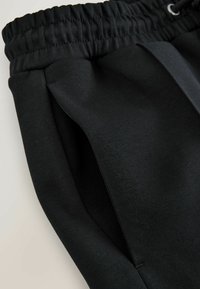 Black sweatpants with an elastic waistband and drawstring. Features front pleats and a smooth, soft texture. Simple, streamlined design.