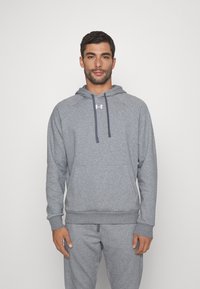 Haut à capuche gris en matériau doux, avec une poche kangourou, un cordon de serrage à la capuche et des poignets côtelés. Logo imprimé sur la poitrine.