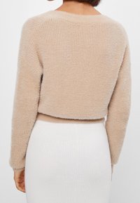 Beige, nadýchaný svetr s kratším střihem a dlouhými rukávy, se žebrovanou strukturou na lemu a manžetách, zobrazený zezadu.