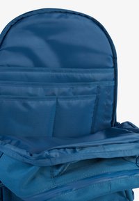 Notranjost modrega nahrbtnika, ki ima več blazinastih žepov in mehko podlogo, narejen iz trpežnega materiala z teksturirano površino.