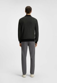 Dark grey knitted sweater with a ribbed collar and cuffs, paired with light grey trousers and white sneakers, viewed from the back.