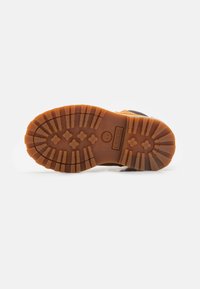 Braune Gummisohle mit tiefen Profilierungen für besseren Halt, mit einem geprägtem Logo an der Ferse, sowie einem Design aus Mischmaterialien mit robuster Konstruktion.