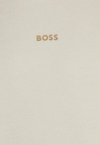 Tejido de color crema con una textura tejida; presenta un pequeño logo dorado de "BOSS" situado en el centro de la superficie.