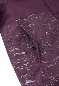 Giacca bordeaux con una texture liscia, dotata di una tasca con zip e un motivo ondulato bianco. Dettagli della zip e del logo visibili sul tessuto.