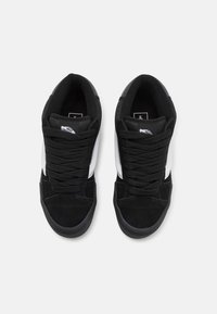 Sneakers in bianco e nero con tomaia in suede e mesh, lacci neri piatti, suola in gomma e striscia laterale bianca.