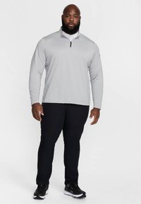 Világosszürke, hosszú ujjú, negyed cipzáras felső, fekete testhez álló nadrág és fekete sportcipő. Simaságot sugárzó anyag, laza szabás, minimális dizájnelemekkel.