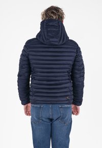 Marine blauwe pufferjack met een capuchon, met een gestikte textuur en zichtbare stiksels. Gepaarde met denim jeans, die een relaxte pasvorm tonen.