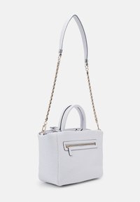 Sac à main tissé blanc avec une bandoulière chaîne dorée, des poignées supérieures et une poche avant zippée sur un fond uni.
