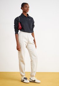 Fekete, hosszúujjas póló a Nike logójával, világosszürke, rugalmas szegélyű és oldalsó varrású melegítőnadrággal, fehér és fekete Nike sportcipővel párosítva.