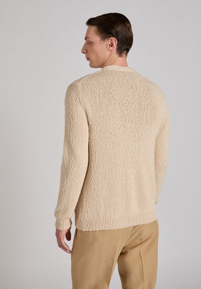 Beige knit sweater with a textured surface, round neck, and long sleeves, paired with light-colored trousers, shown from the back view.