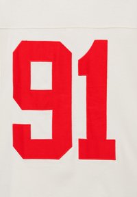 Numéro rouge "91" imprimé sur un tissu blanc, probablement une partie d'un maillot de sport ou d'un uniforme.