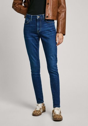 Jean en denim bleu skinny à taille haute, avec cinq poches et des coutures contrastées. Associés à des baskets à imprimé léopard.