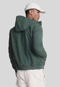 Groene hoodie gemaakt van gladde stof, met een ritssluiting, zakken aan de zijkant en geribde boorden bij de polsen en zoom.