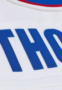Weißer Stoff mit kräftig gestickten blauen Buchstaben und strukturierter Oberfläche. Ein roter Akzent verläuft entlang der oberen Kante des Designs.