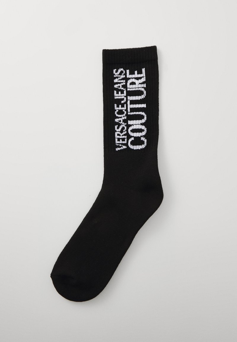 Black sock with ribbed texture, featuring "VERSACE JEANS COUTURE" in white embroidery on the side. Classic crew length design.