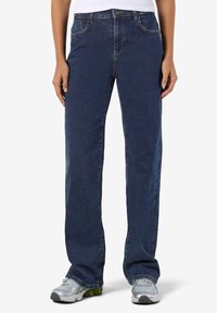 Tmavě modré džíny s rovnými nohavicemi, pěti kapsami a kontrastním šitím. Nošeny s světle šedými sportovními botami.