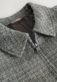 Gray wool jacket with a structured collar, diagonal zipper, and textured fabric featuring a subtle pattern. Inner lining is dark gray.