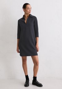 Ciemnoszara sukienka do kolan z kołnierzykiem polo i rękawami o długości trzy czwarte. Gładki materiał z bocznymi rozcięciami. W zestawie z czarnymi butami na platformie.