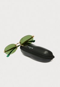 Occhiali da sole con tonalità verde e dettagli in oro, dalla forma ovale. Include una custodia nera con zip con il logo "vogue" sul fronte.