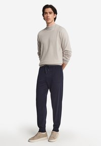 Ljusgrått polotröja och marinblå dragkedjebyxor, tillsammans med beige sneakers. Mjuka texturer och avslappnad passform.