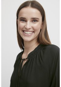 Juoda bliuskutė su apvaliu iškirptimu, susiraukimo detalėmis, susirišimo uždanga ir laisvas įgula. Sklandus paviršius ir lengvas audinys.