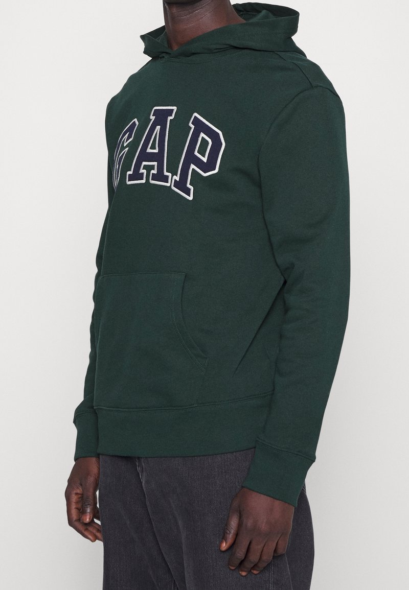 Groene hoodie met "GAP" in wit en marineblauw op de borst, voorzien van een voorzak in kangoeroestijl en geribbelde boorden.