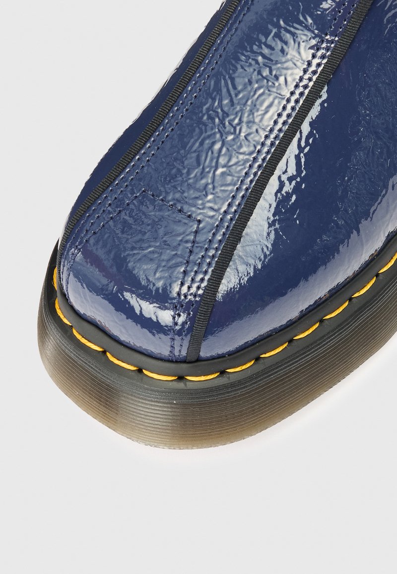 Stivale alla caviglia blu navy con una tomaia lucida e testurizzata, dotato di pannelli elastici laterali e una welt cucita gialla su una suola in gomma nera.