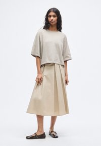 Pull court gris clair, jupe midi plissée beige et chaussures plates marron. Textures douces, coupe décontractée et design simple sans motifs.