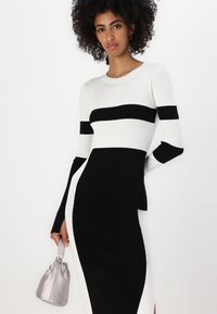 Svart och vit ribbad klänning med långa ärmar, som har horisontella ränder och en figurnära siluett. Accenterad av en silvrig väska.