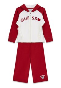 Roter und weißer zweiteiliger Trainingsanzug mit Reißverschluss-Hoodie, Rüschendetails und "GUESS"-Logo aus Strasssteinen, kombiniert mit passenden roten Hosen.