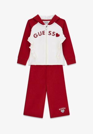Dwuczęściowy dres w kolorze czerwono-białym z bluzą zapinaną na zamek z kapturem, ozdobiony falbankami i logo "GUESS" z kamieniami szlachetnymi, w komplecie z pasującymi czerwonymi spodniami.