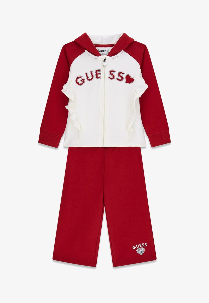 Roter und weißer zweiteiliger Trainingsanzug mit Reißverschluss-Hoodie, Rüschendetails und "GUESS"-Logo aus Strasssteinen, kombiniert mit passenden roten Hosen.