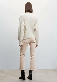Pull en tricot côtelé ivoire avec épaules tombées, associé à un jean coupe évasée rose clair et des bottes à talons noires, vu de derrière.