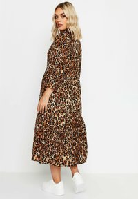 Leopardi-kuosi midi-mekko lämpimissä ruskeissa ja vaaleanbeigeissä sävyissä, jossa on kerroksellinen hame ja väljät hihat, yhdistettynä valkoisiin tennareihin.